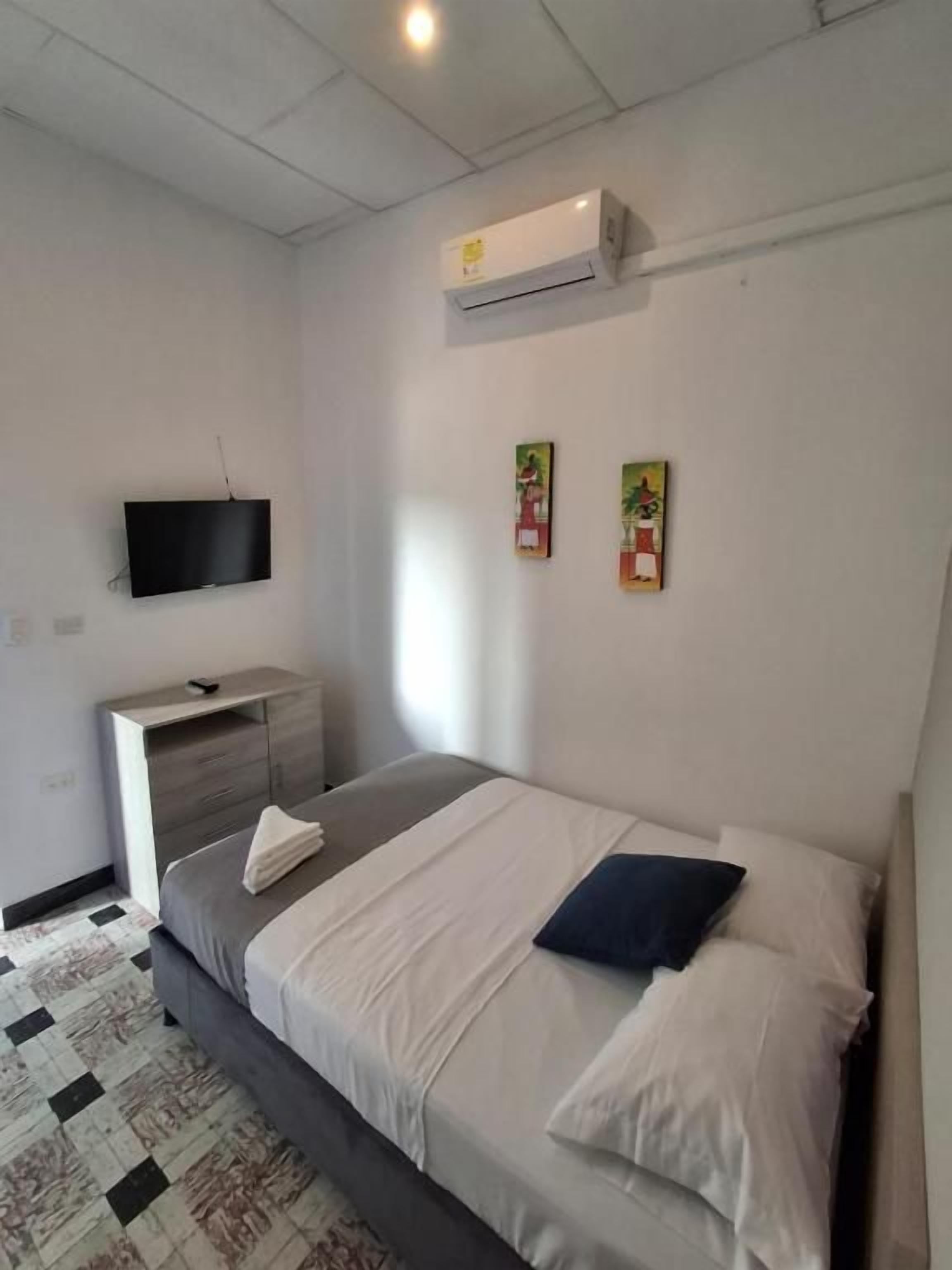 A bedroom with a bed, a bedside table, a TV mounted on the wall, and a wall-mounted air conditioner.