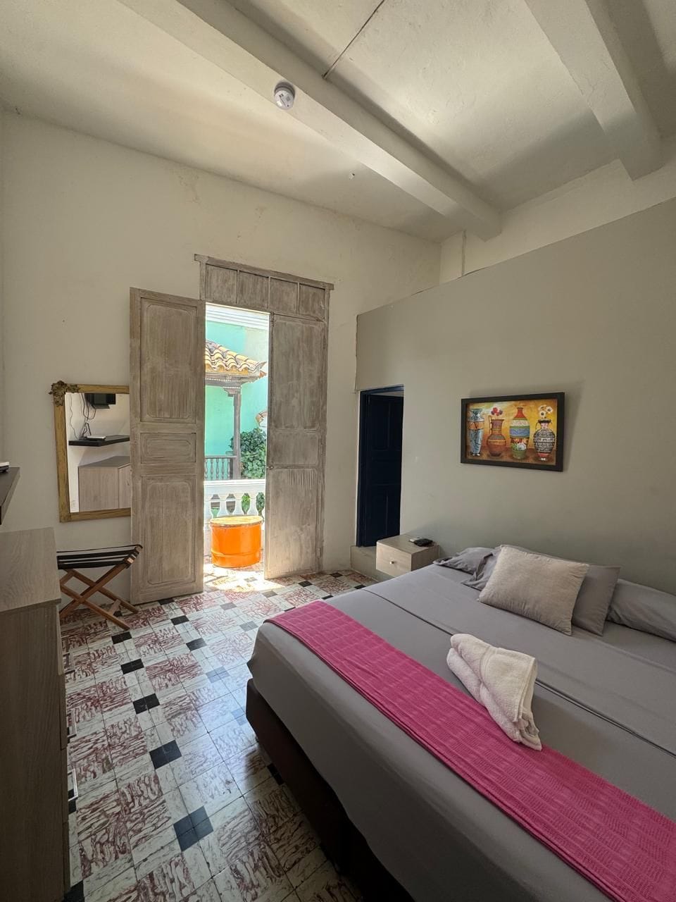 Een slaapkamer met een bed, een bureau, een stoel, een raam en een deur die leidt naar een buitenruimte.