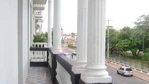 A balcony with white columns and a black balustrade, overlooking a street with cars and greenery. - Casa 1811 (Cartagena)
