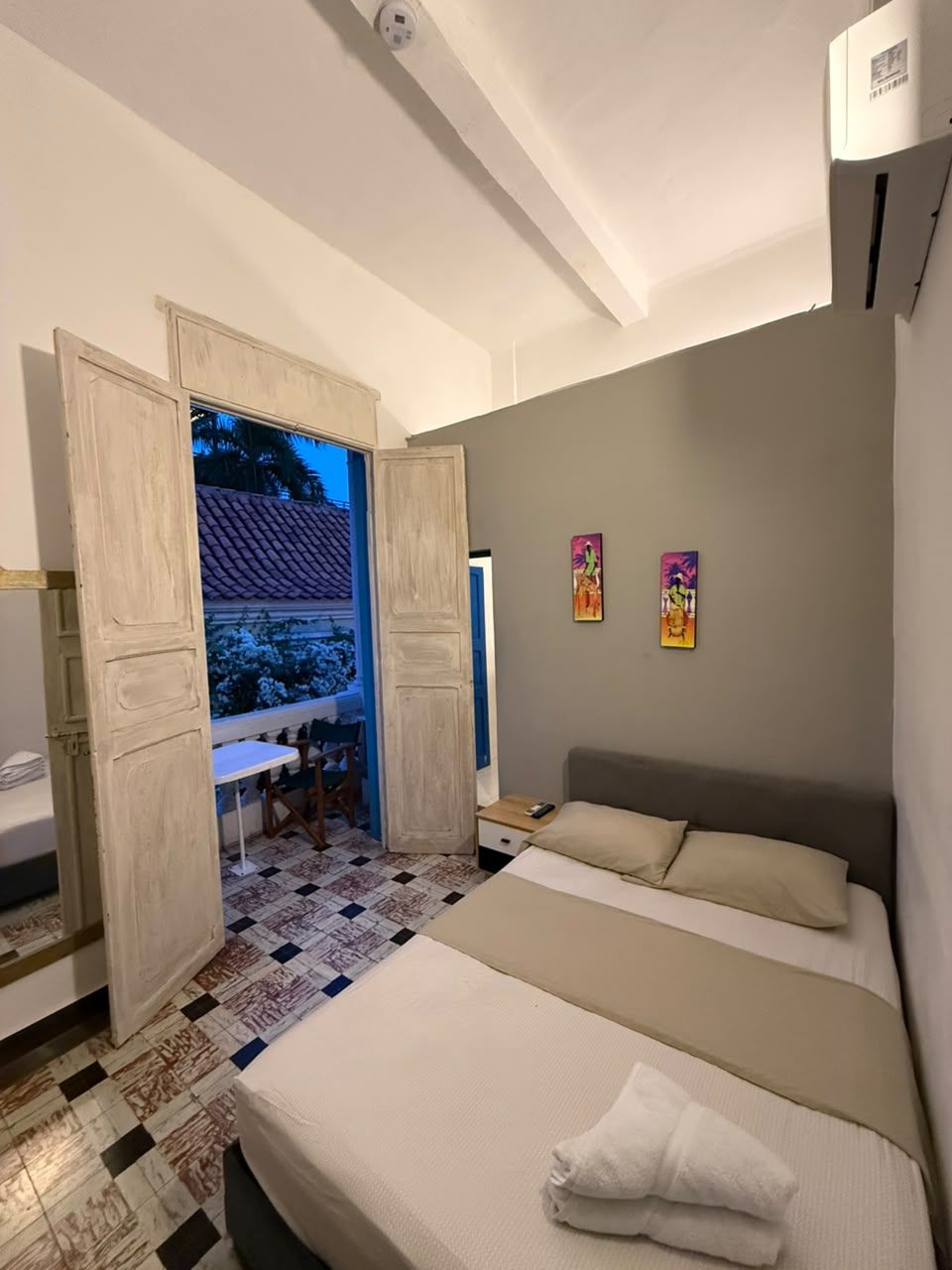 A bedroom with a bed, a nightstand, a window with a view, and two wall art pieces.