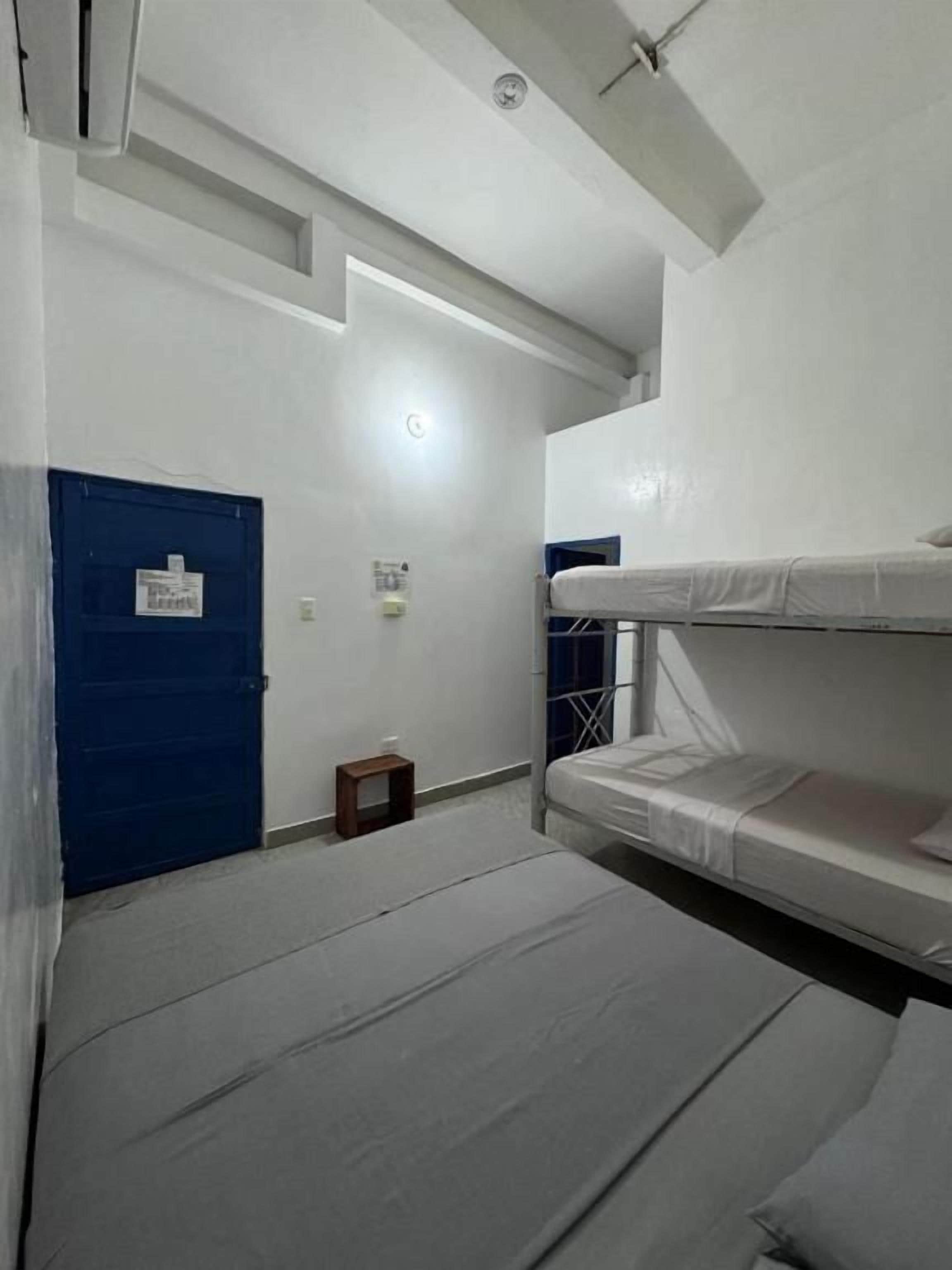 Una habitación con literas, una puerta azul y una mesita.