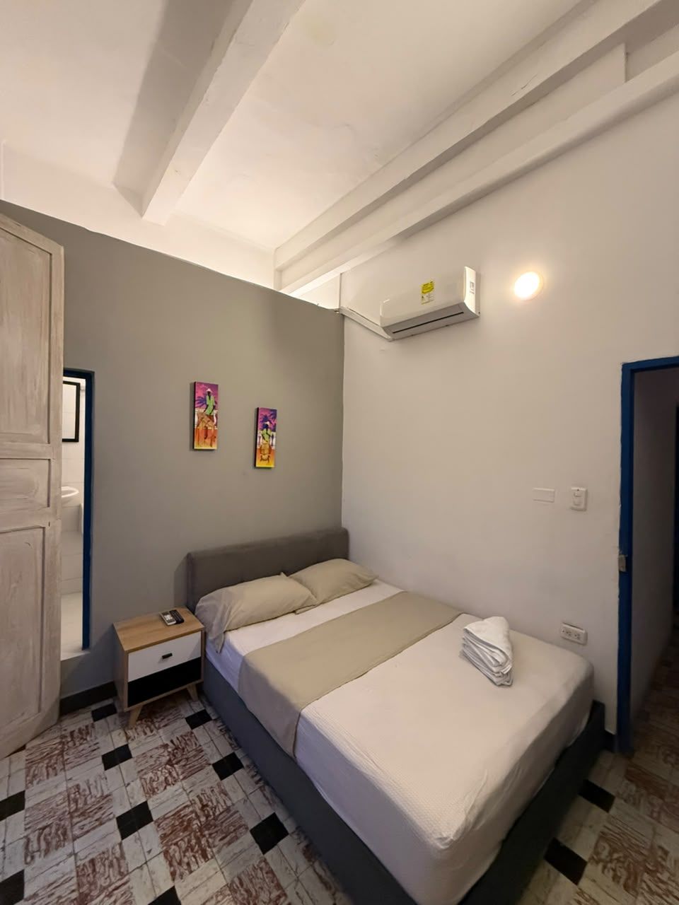 A bedroom with a bed, a nightstand, a wall-mounted air conditioner, and two wall-mounted light fixtures.
