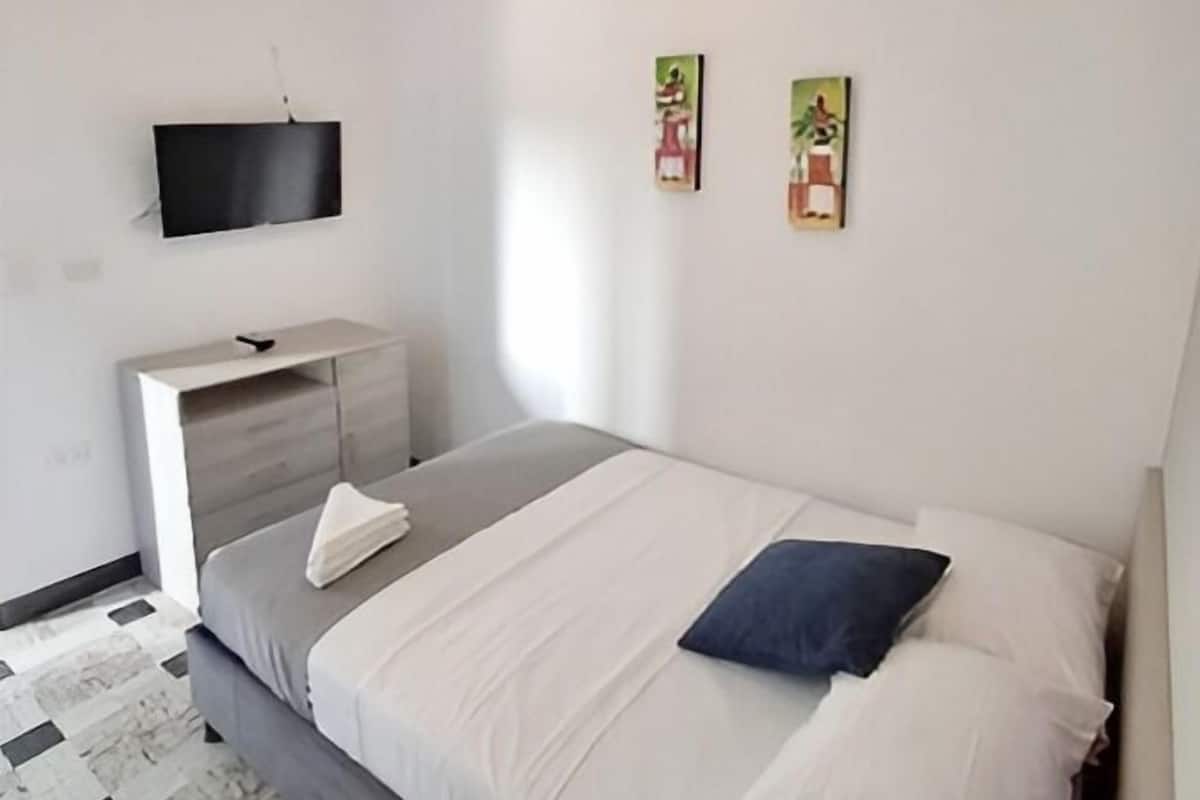 Quarto moderno com cama, televisão de tela plana na parede e uma pequena mesa de cabeceira.