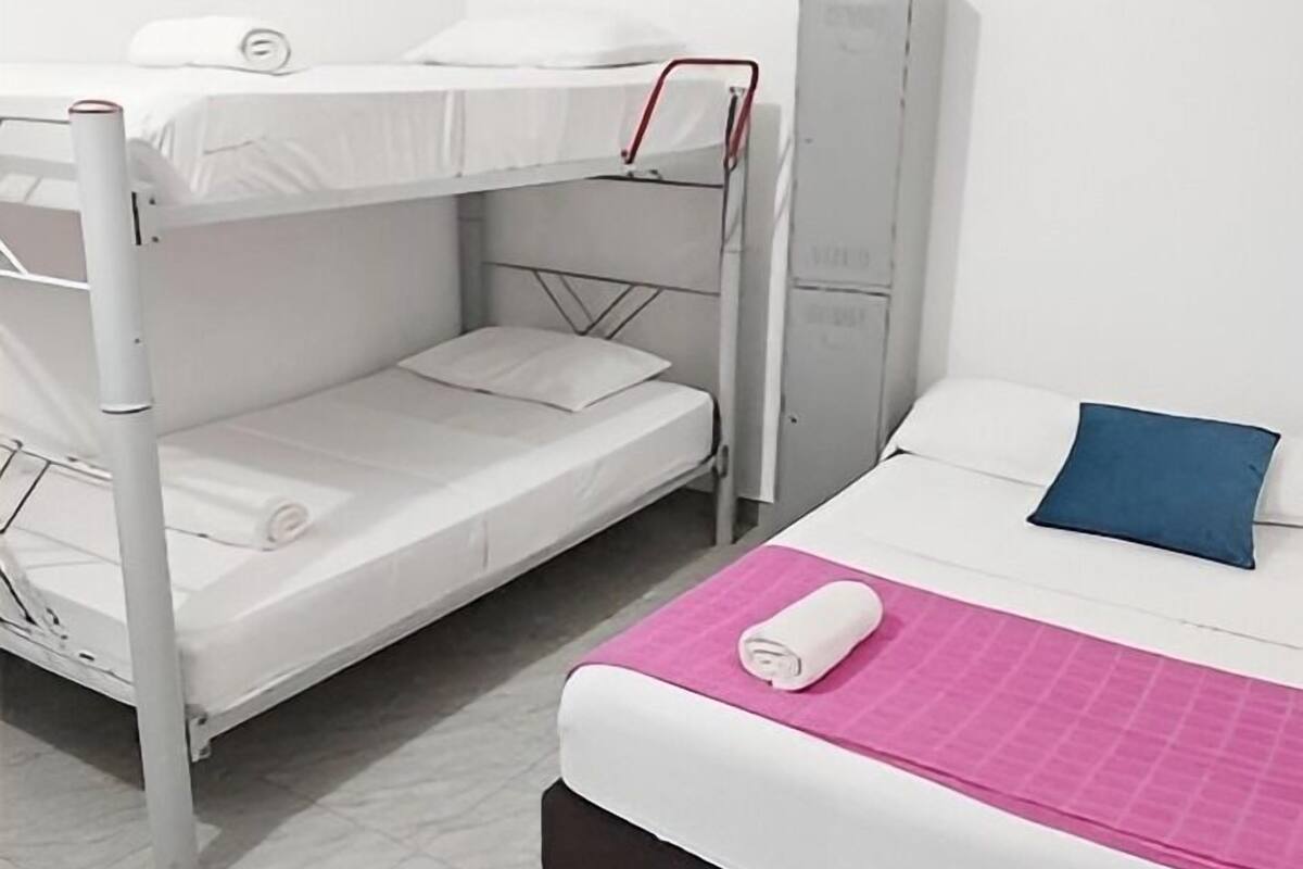 Uma cama de solteiro com colchão branco e beliche inferior com estrutura de metal.