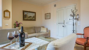 A living room with a glass coffee table, beige sofa, and a door with a decorative iron handle. - Efeso (Florence)