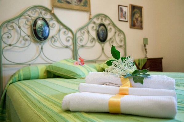 Una cama bien hecha con ropa de cama verde a rayas, un cabecero de metal decorativo y un pequeño ramo de flores blancas.