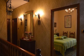 A hotel room with a wooden staircase, a bed with green bedding, a nightstand, a mirror, and wall sconces.