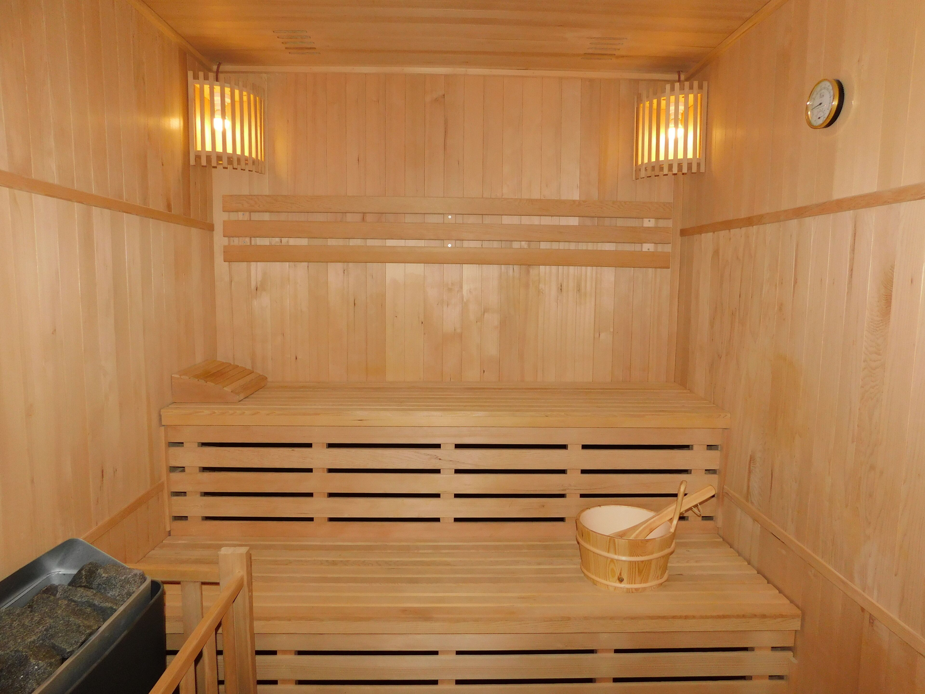 Una sauna de madera con bancos, un cubo de madera y luces fijadas a la pared.