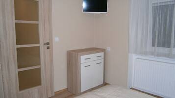 Quarto com guarda-roupa de madeira, televisão na parede e janela com cortinas leves.