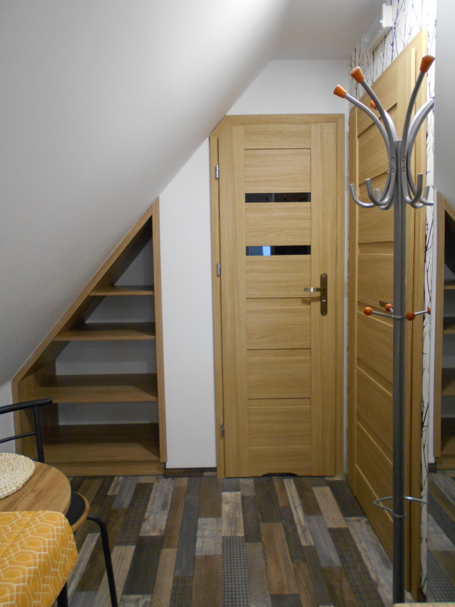 A room with a wooden door, a coat rack, and a staircase leading to an upper level.