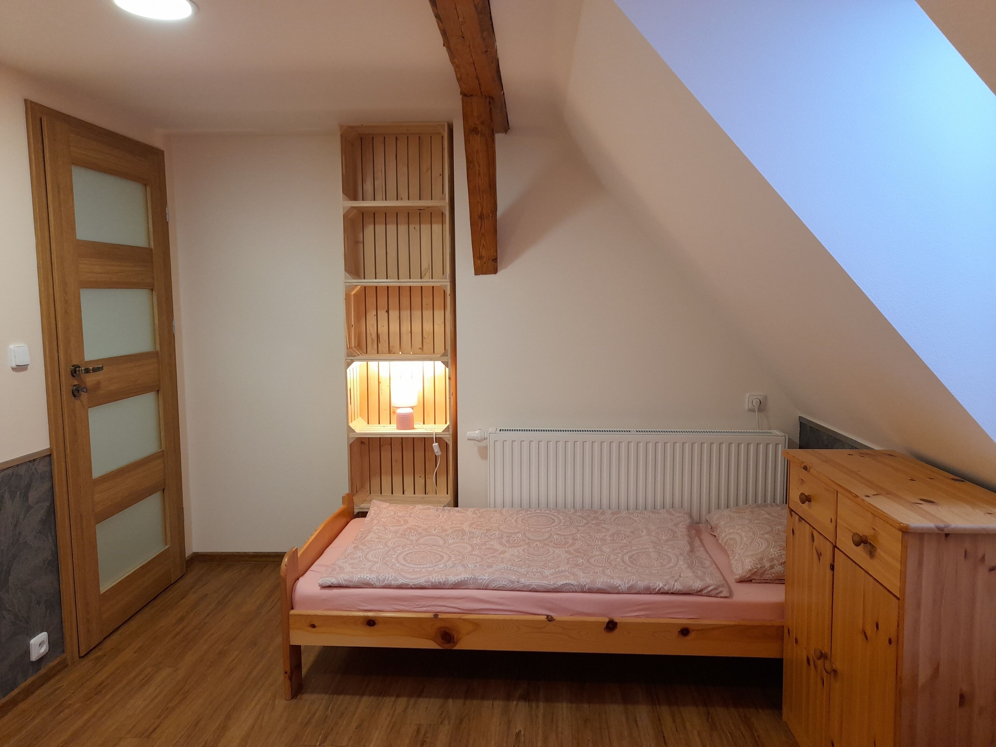 Quarto com cama de madeira, estante embutida, radiador e teto inclinado.