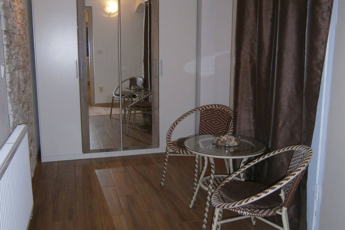 A small, open-plan living area with a wooden floor, a glass door leading to a balcony, wicker furniture, and a brown curtain.