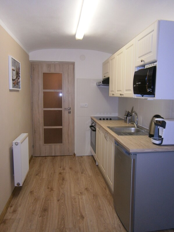 A compact kitchen with wooden flooring, white cabinets, a microwave, a coffee maker, and a double sink.