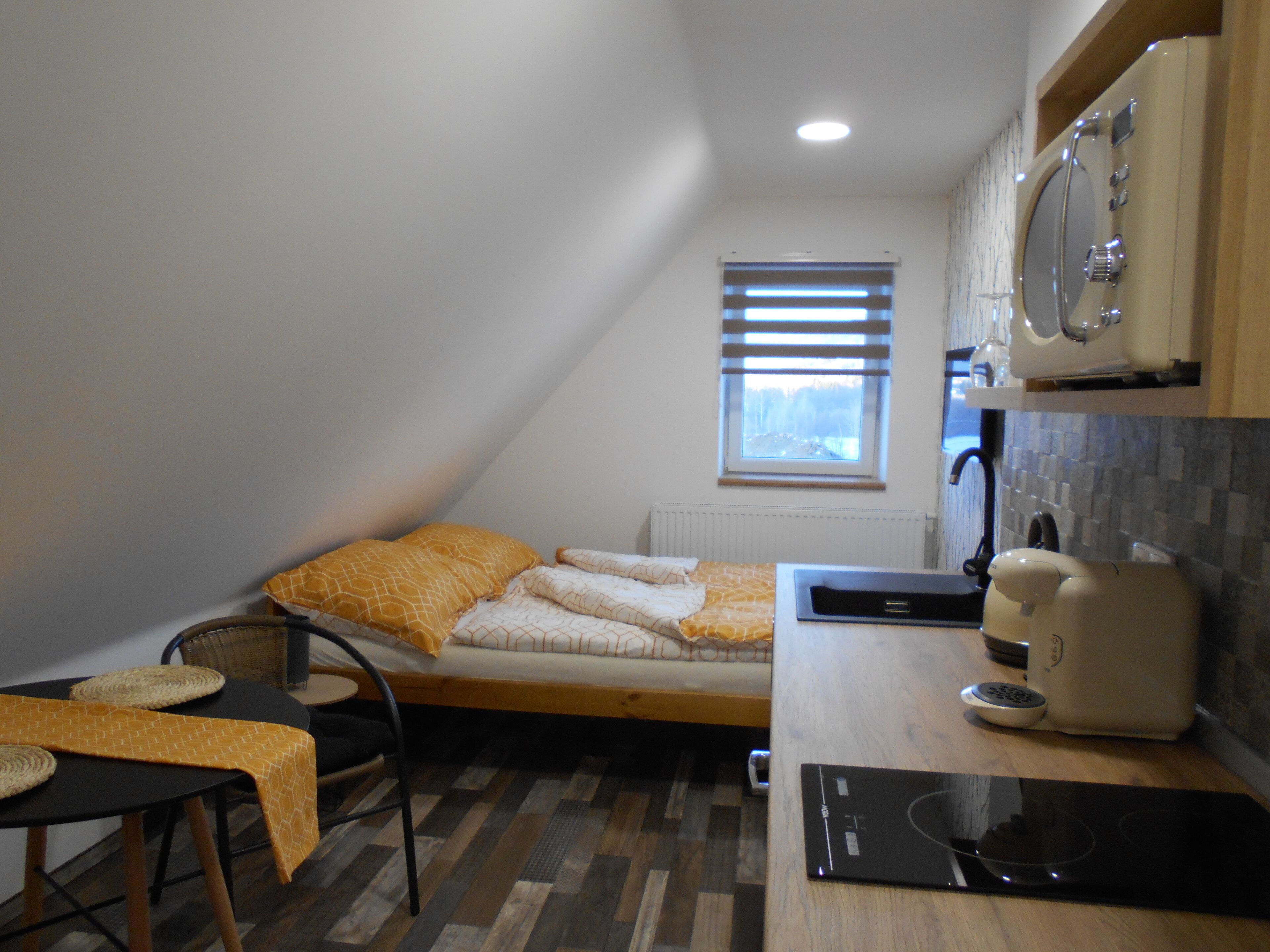 Una habitación pequeña y funcional con cama, mesa, hervidor y microondas.