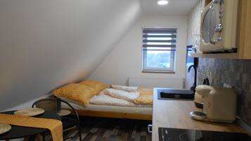 Una habitación pequeña y funcional con cama, mesa, hervidor y microondas.