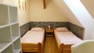 A small, cozy room with two wooden beds, a white chair, and a bookshelf.