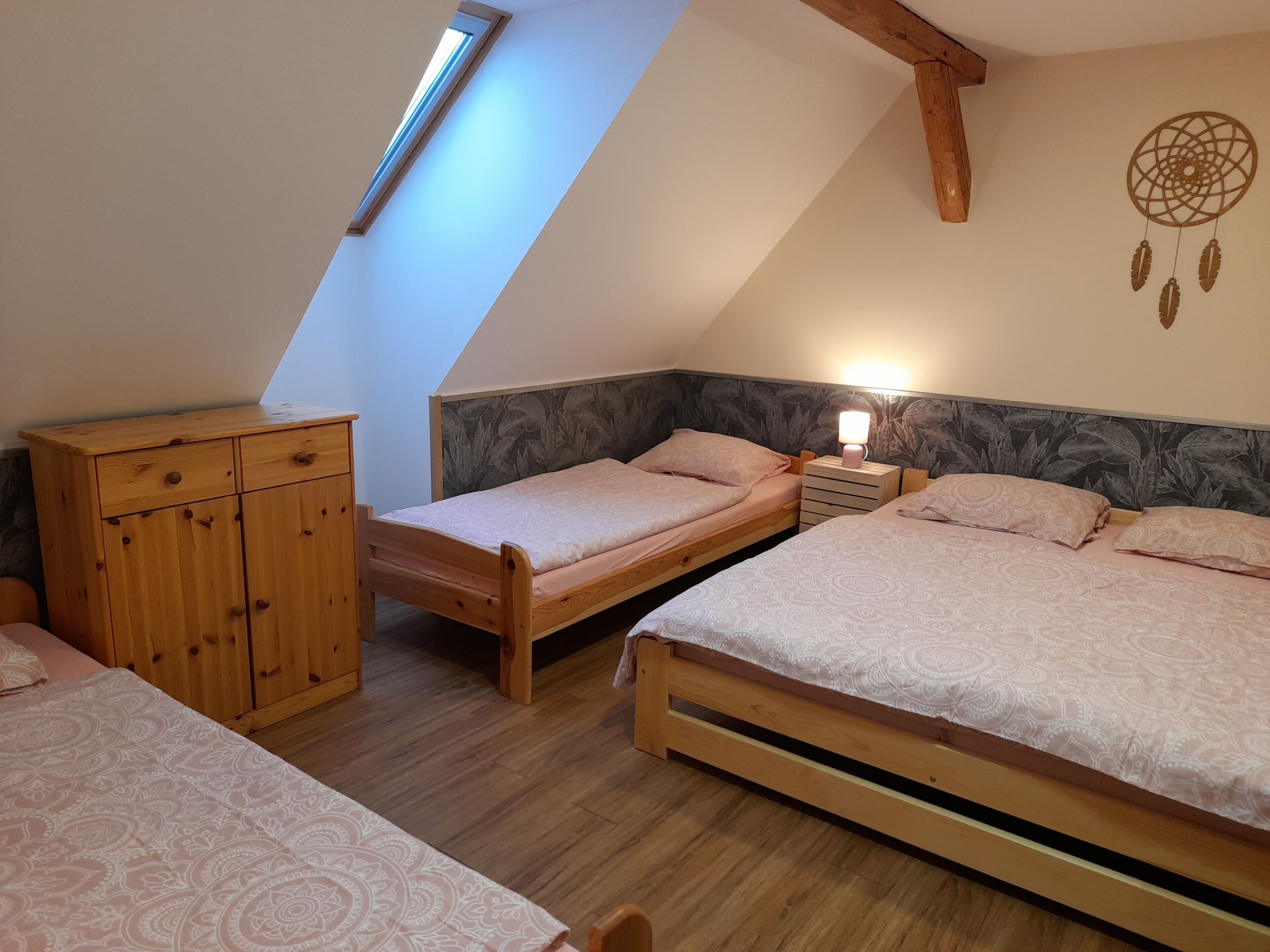Un dormitorio con dos camas, un armario de madera, un tragaluz y un atrapasueños en la pared.
