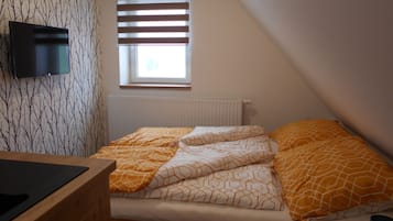 Une chambre à coucher avec un lit, une fenêtre avec des stores, un radiateur et un téléviseur fixé au mur.