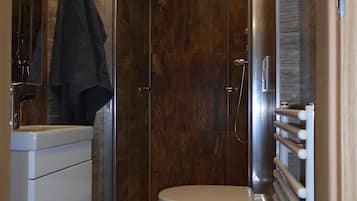A modern bathroom with a glass-enclosed shower, a toilet, and a built-in sink.