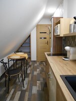 Cocina compacta con encimera de madera, microondas y tostadora. Pequeño comedor con dos sillas y una mesa.