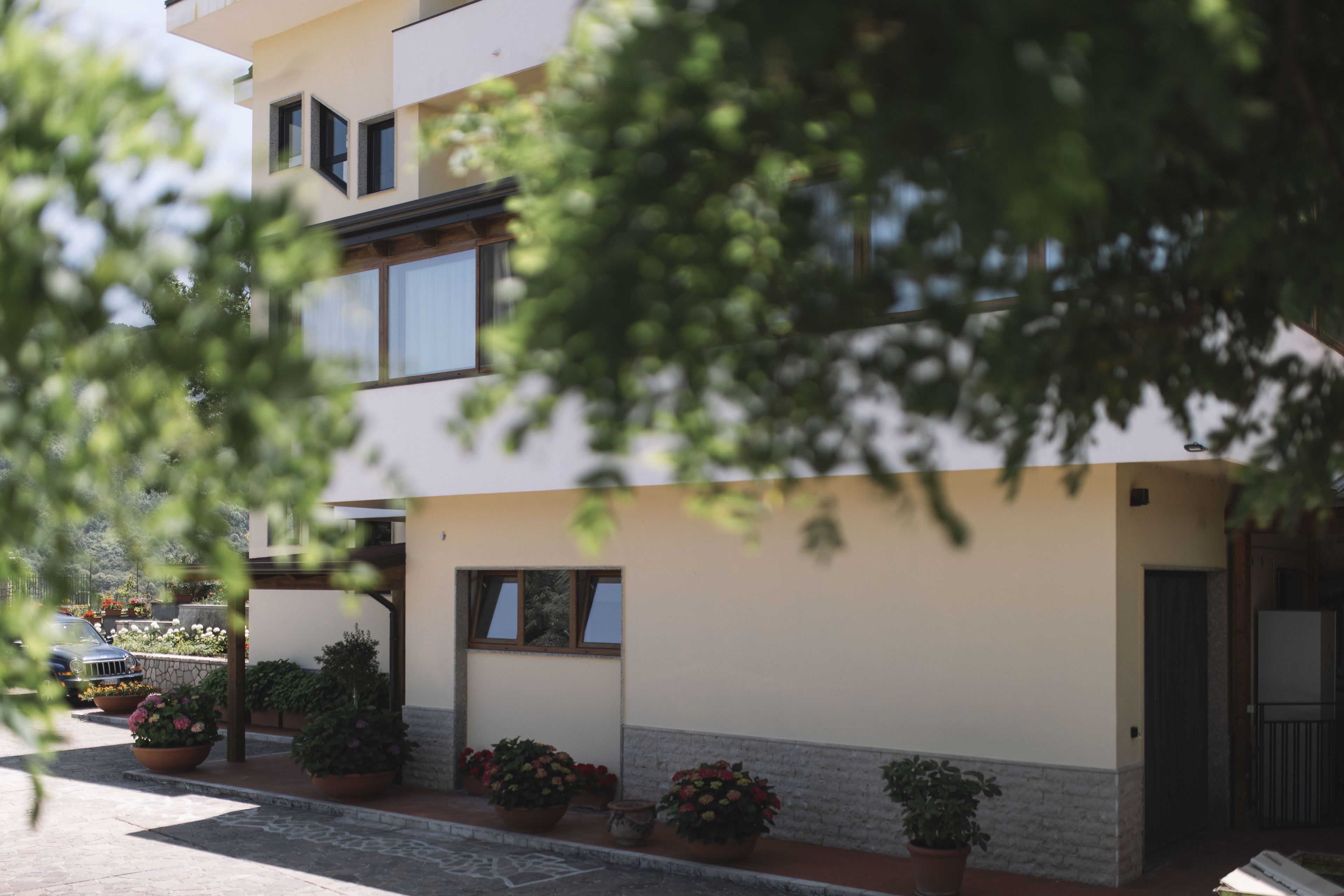 Un edificio moderno de dos plantas con techo plano y un balcón. Hay plantas y flores en macetas en la planta baja.