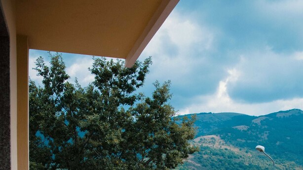 A balcony with a wicker chair, potted red flowers, and a view of green hills. - La Villa Resort Charme & Relax (Pignola)