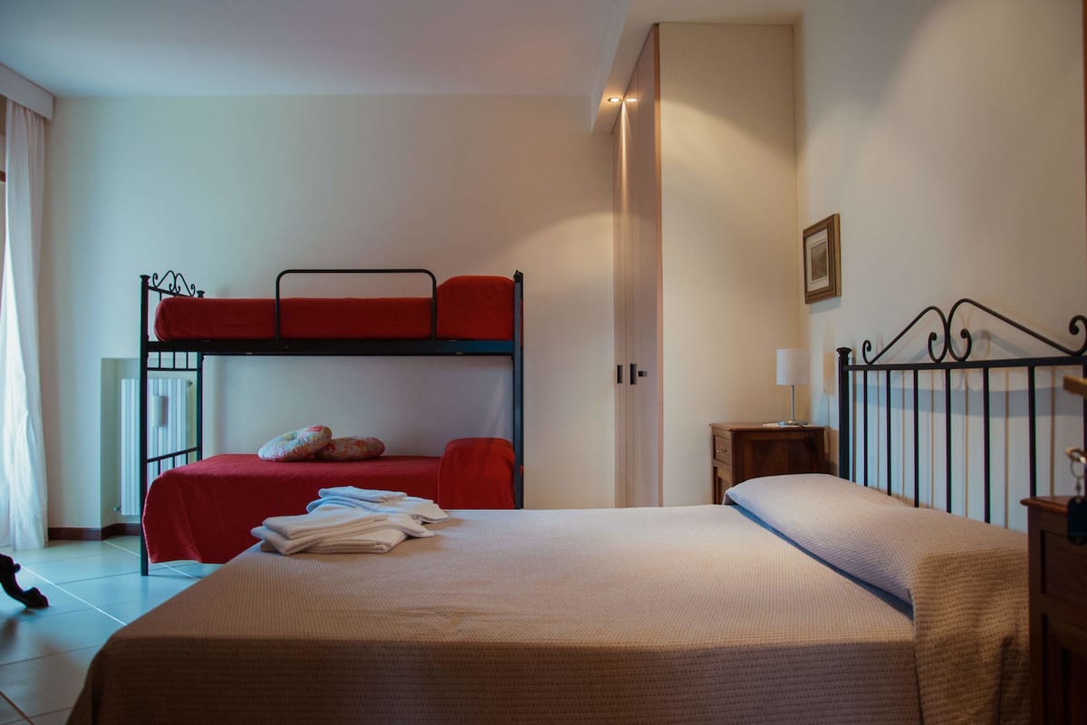 A room with a bunk bed, a single bed, a bedside table with a lamp, and a small cabinet.