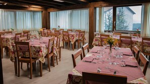 A dining area with multiple tables set for meals, wooden beams on the ceiling, and large windows with curtains. - La Villa Resort Charme & Relax (Pignola)