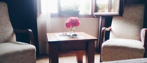 A room with two armchairs, a small table with a vase of flowers, and a window providing natural light.