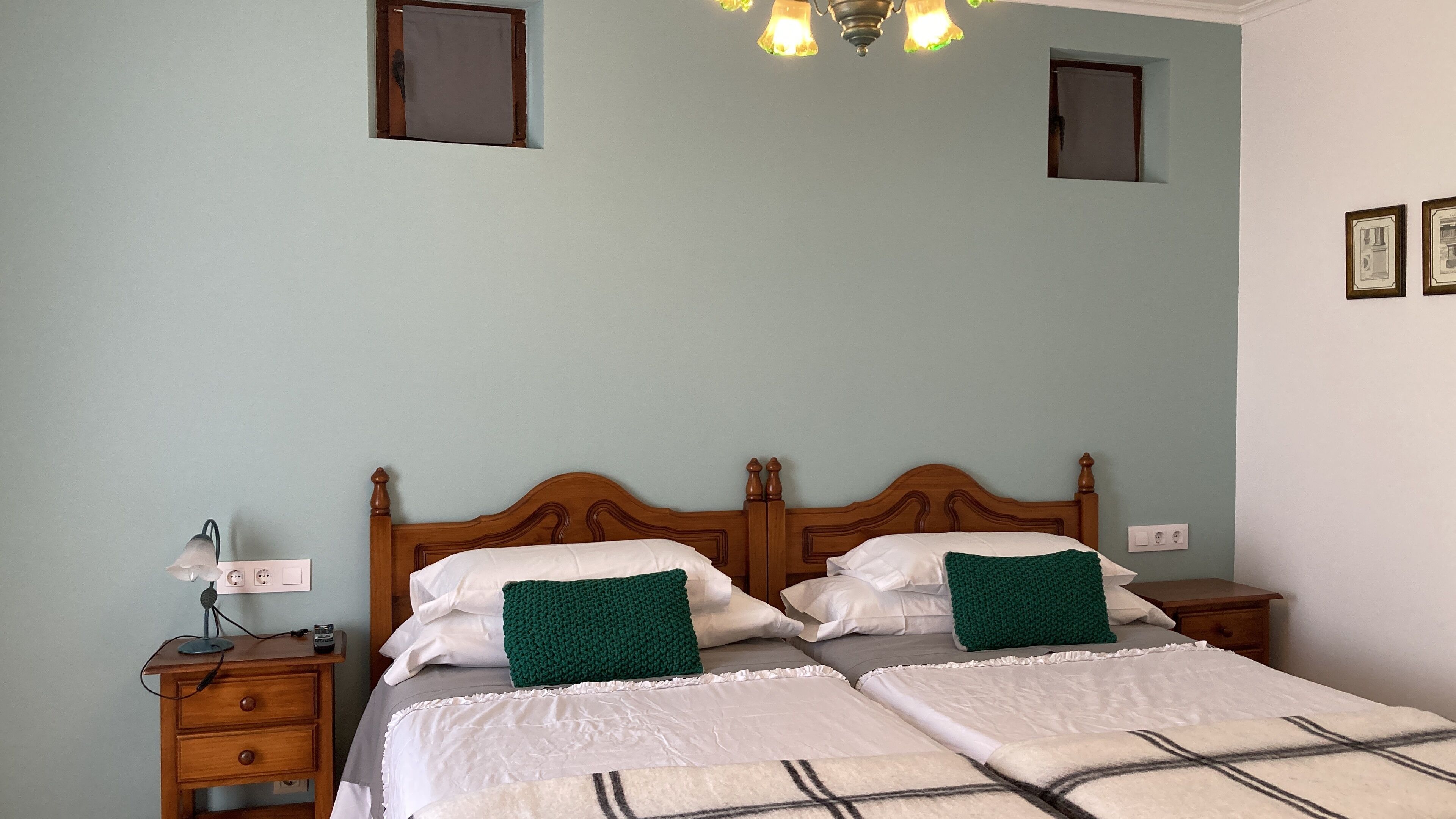Una cama doble con dos almohadas, una mesita de noche con lámpara y una lámpara de pared.