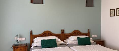 Una cama doble con dos almohadas, una mesita de noche con lámpara y una lámpara de pared.