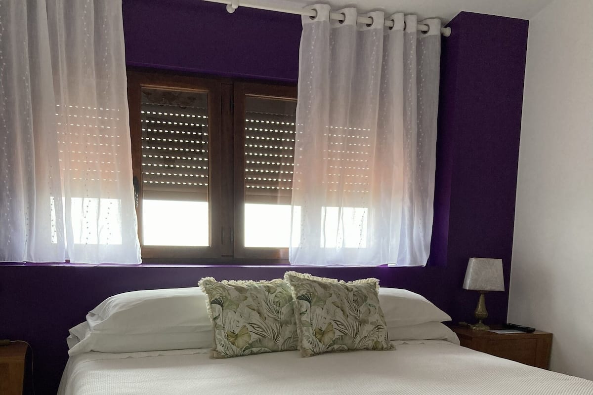 A bedroom with a bed, two nightstands, a lamp, and a window with curtains.