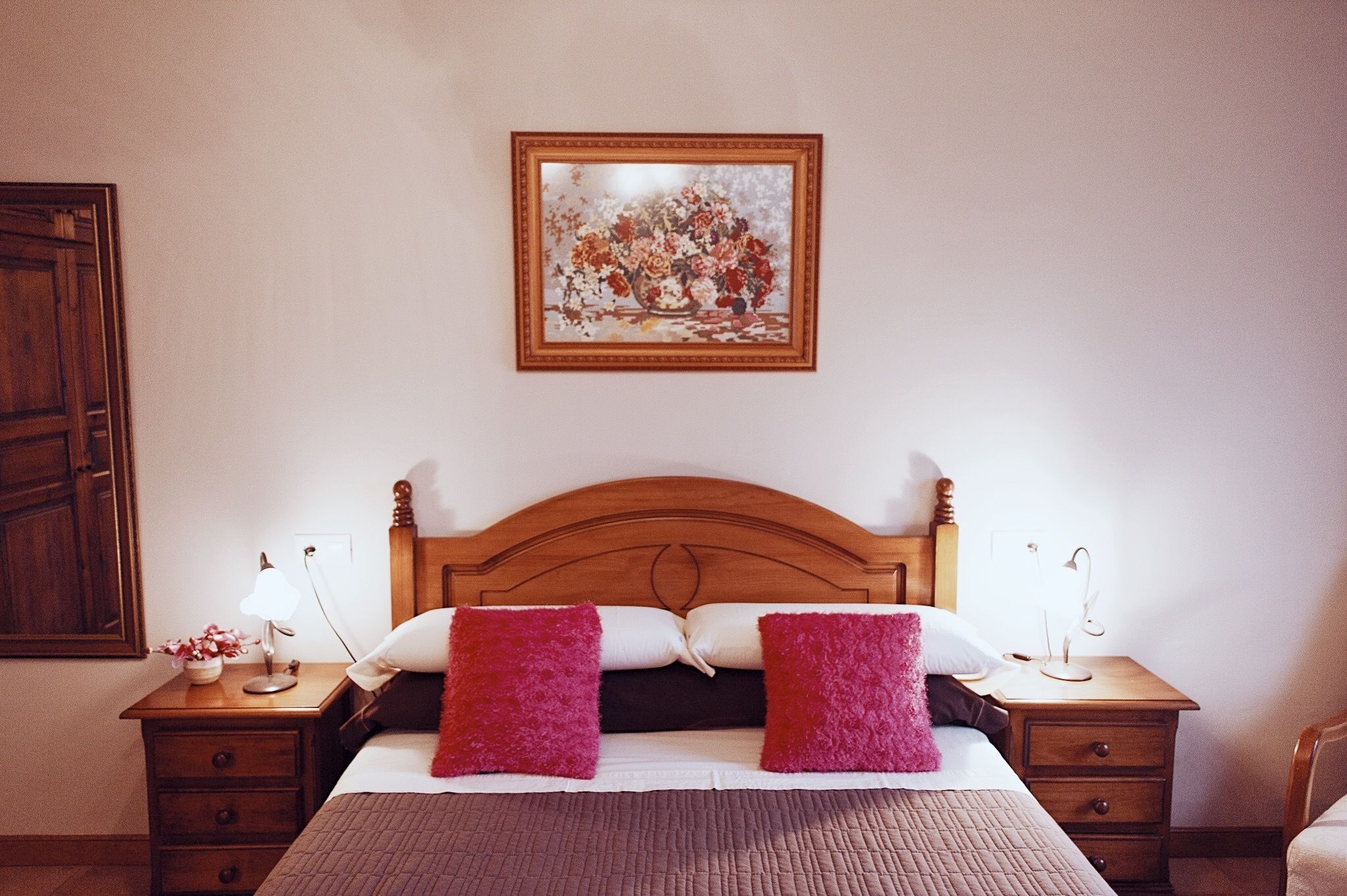 Ein ordentlich eingerichtetes Schlafzimmer mit einem hölzernen Kopfteil, einem Nachttisch mit Lampe sowie einem weiteren Nachttisch mit Lampe und einem gerahmten Bild an der Wand.