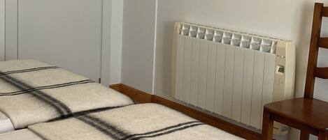 Un dormitorio con una cama, un radiador, una puerta y un cuadro en la pared.