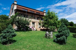 Una casa de dos pisos con fachada de piedra, un balcón con plantas en macetas y un jardín bien cuidado con arbustos y flores variados.