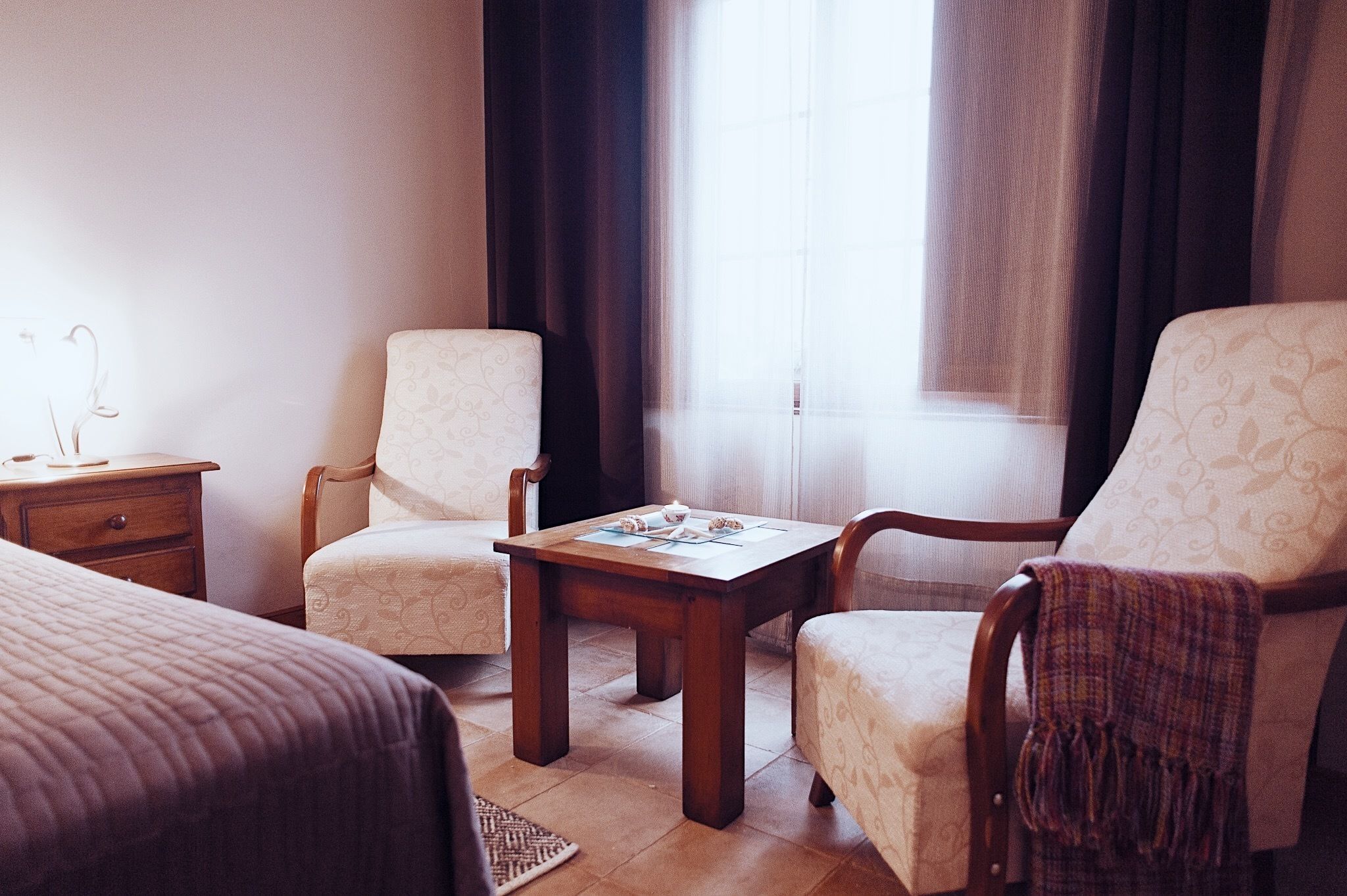 Una habitación de hotel con una cama, dos sillones, una mesa de madera y una mesita de noche.