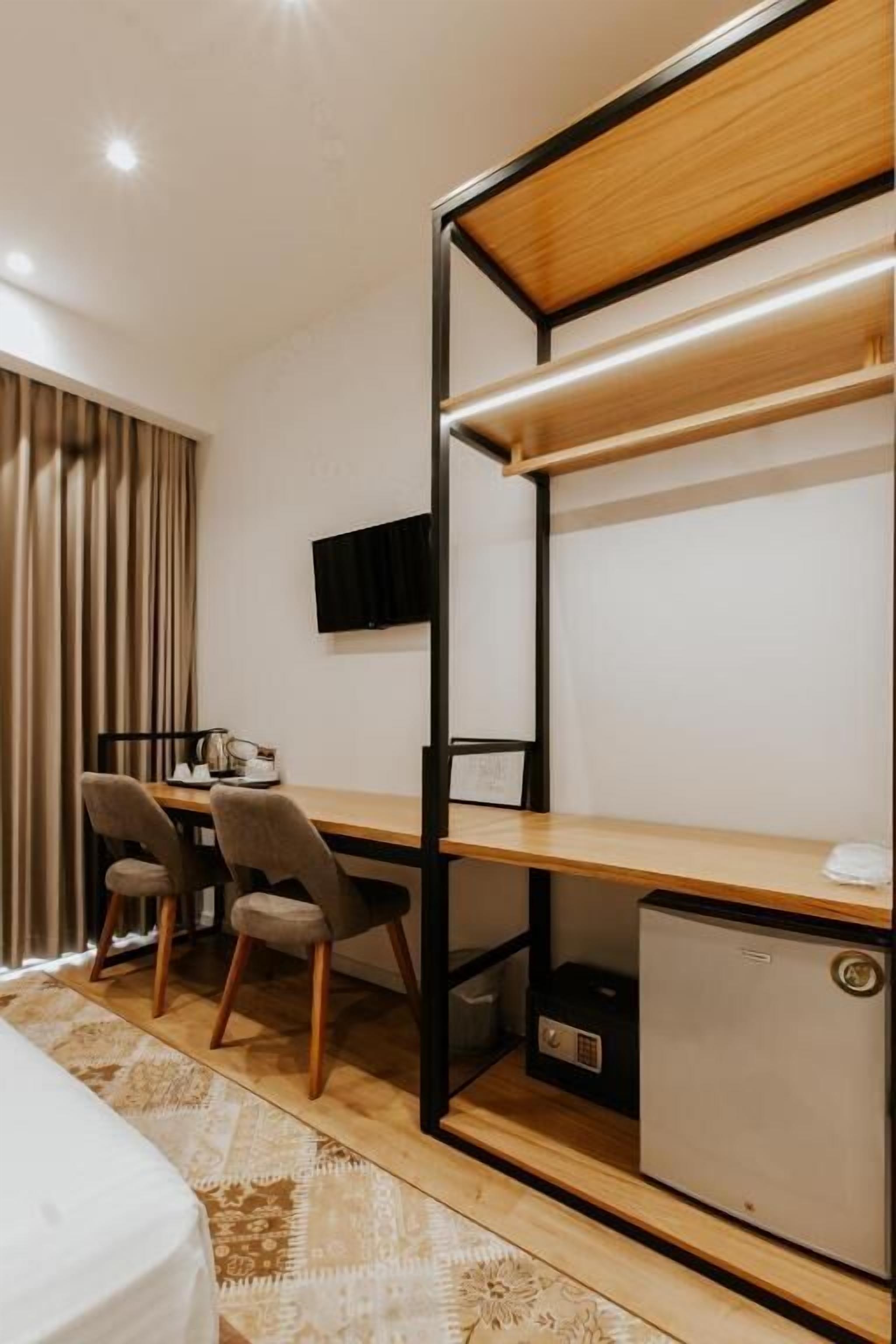 A compact hotel room with a bed, a desk with chairs, a television, and a small refrigerator.