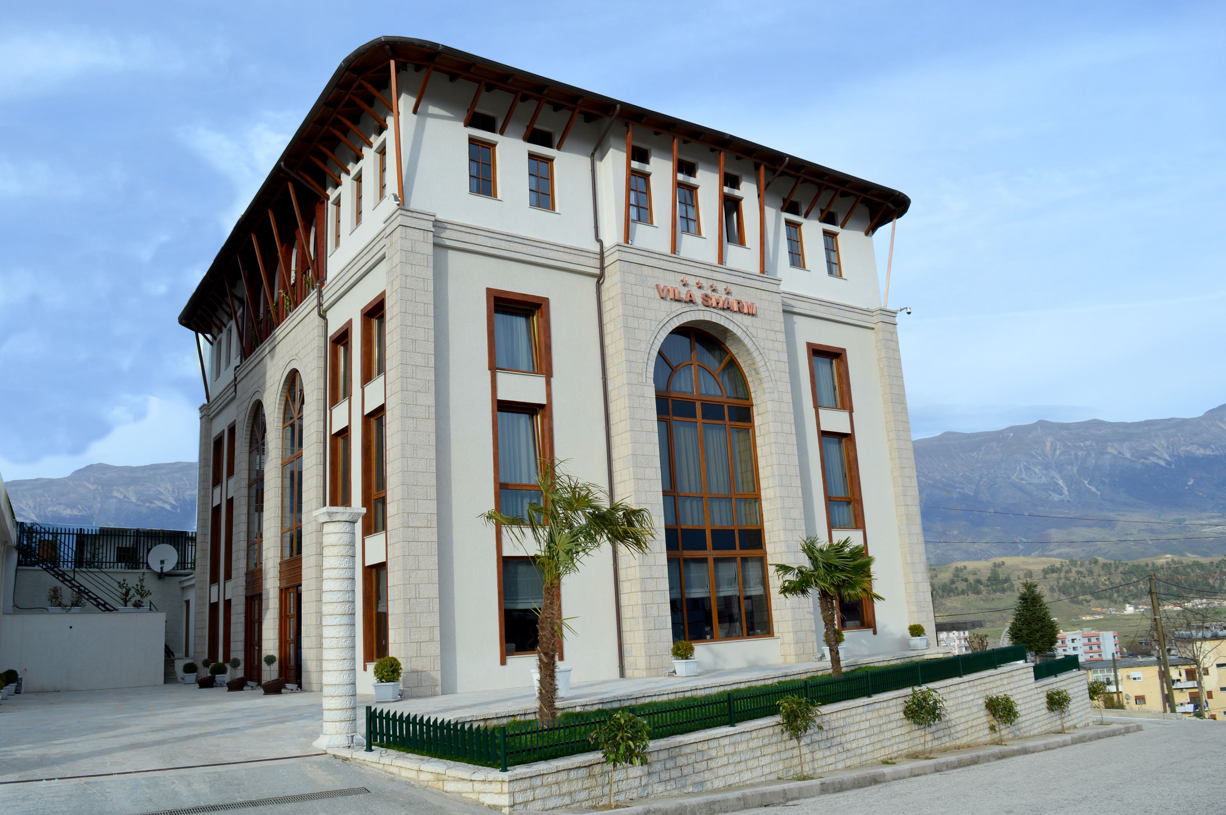 Un bâtiment à la façade blanche, doté de grandes fenêtres en arc de cercle et d’une enseigne sur laquelle on peut lire « Villa Sharm ».