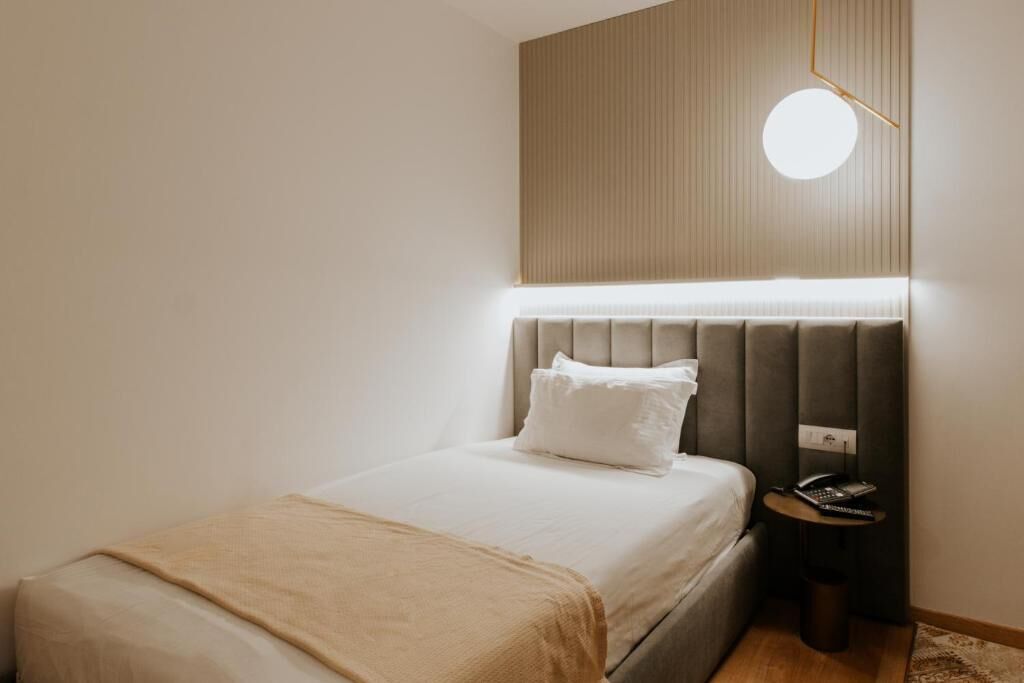 A modern hotel room with a bed, bedside table, and a wall-mounted light fixture.