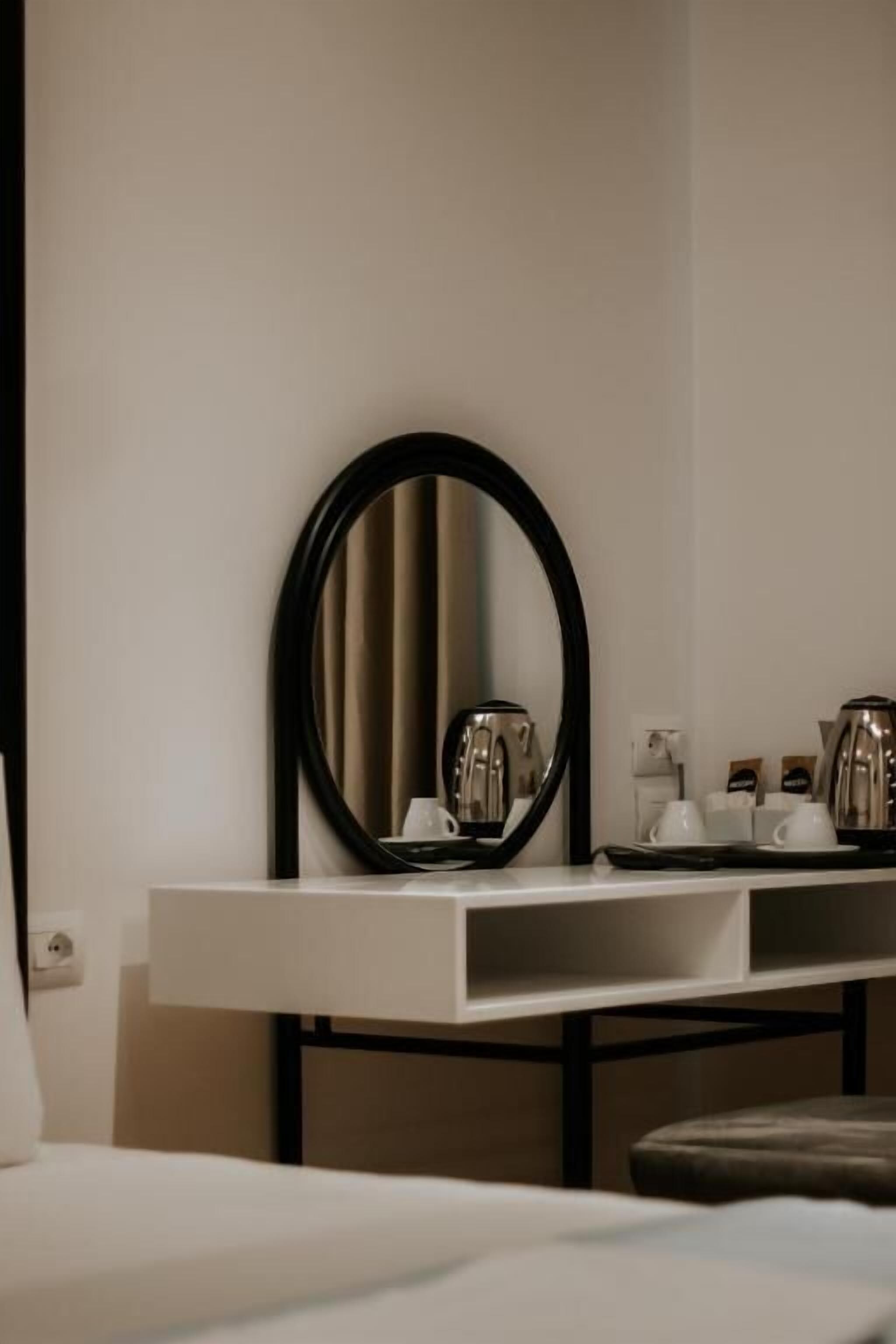 Ein Hotelzimmer mit einem Bett, einem Nachttisch mit Spiegel und einer kleinen Küchenzeile mit Wasserkocher und Tassen.