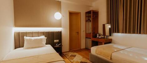 A hotel room with two beds, a wooden headboard, a bedside table, a nightstand, a wardrobe, and a mirror.