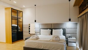 A modern hotel room with a large bed, a walk-in closet, bedside tables, and a nightstand. - Sharm Hotel (Gjirokastër)