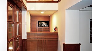 A reception area with a wooden desk, a framed picture of a building, and a flag on the wall. - Sharm Hotel (Gjirokastër)