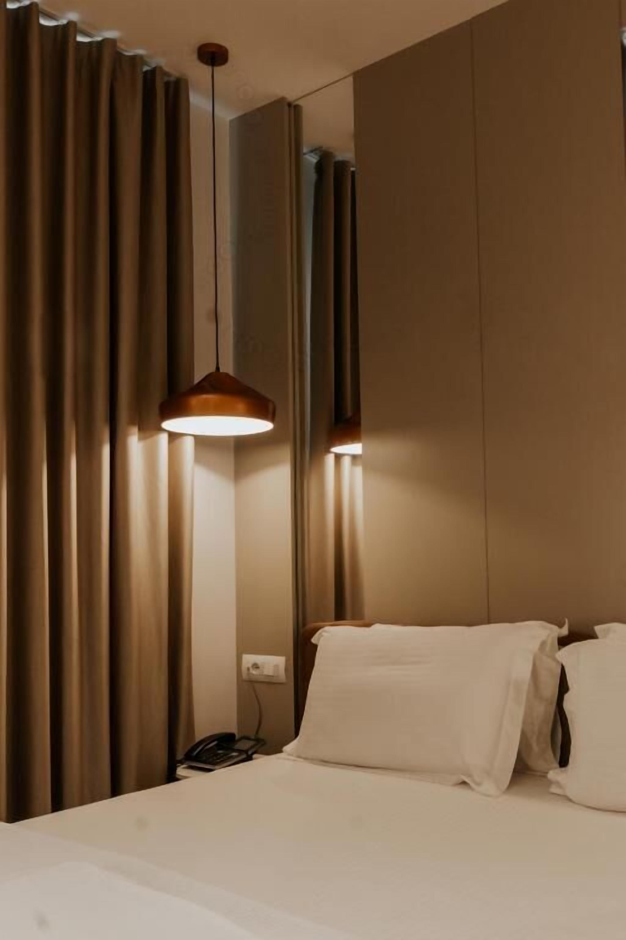 Une chambre d’hôtel avec un lit, des rideaux, un luminaire suspendu et un téléphone.