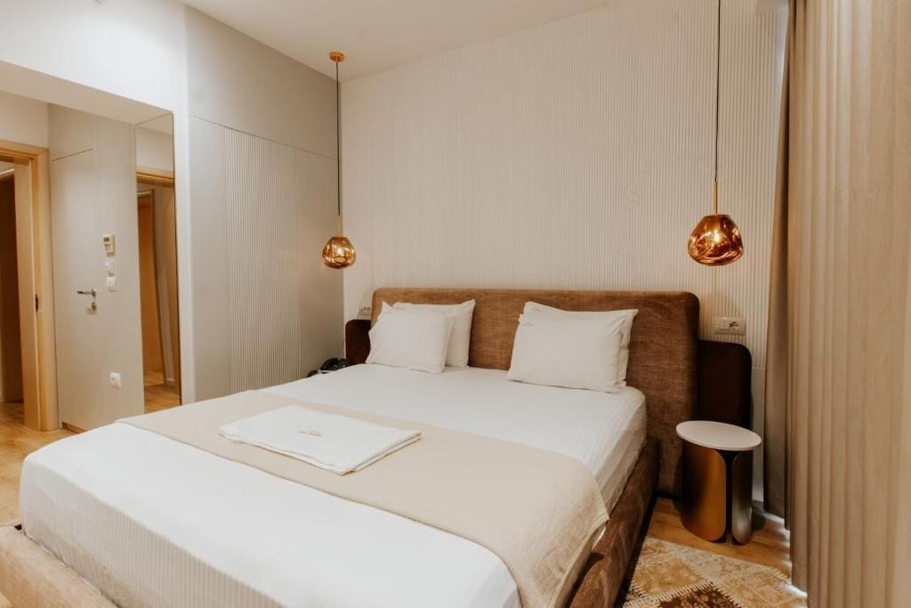 Een moderne slaapkamer met een groot bed, twee nachtkastjes en een kleine ronde tafel.