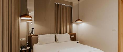Una habitación de hotel moderna con una cama grande, dos lámparas colgantes, una mesita de noche con lámpara y una cortina.