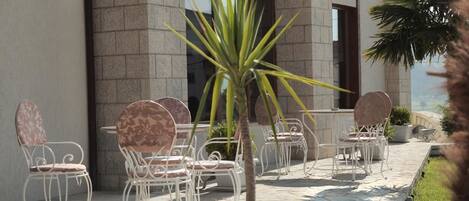 An outdoor seating area with white metal chairs and a central potted plant.