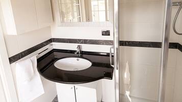 Casa de banho com lavatório branco, bancada preta e cabine de duche em vidro.