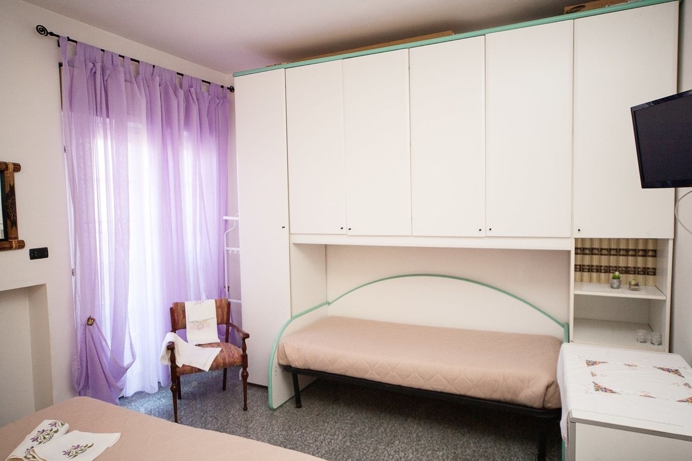 A bedroom with a single bed, a chair, a desk, and a TV.
