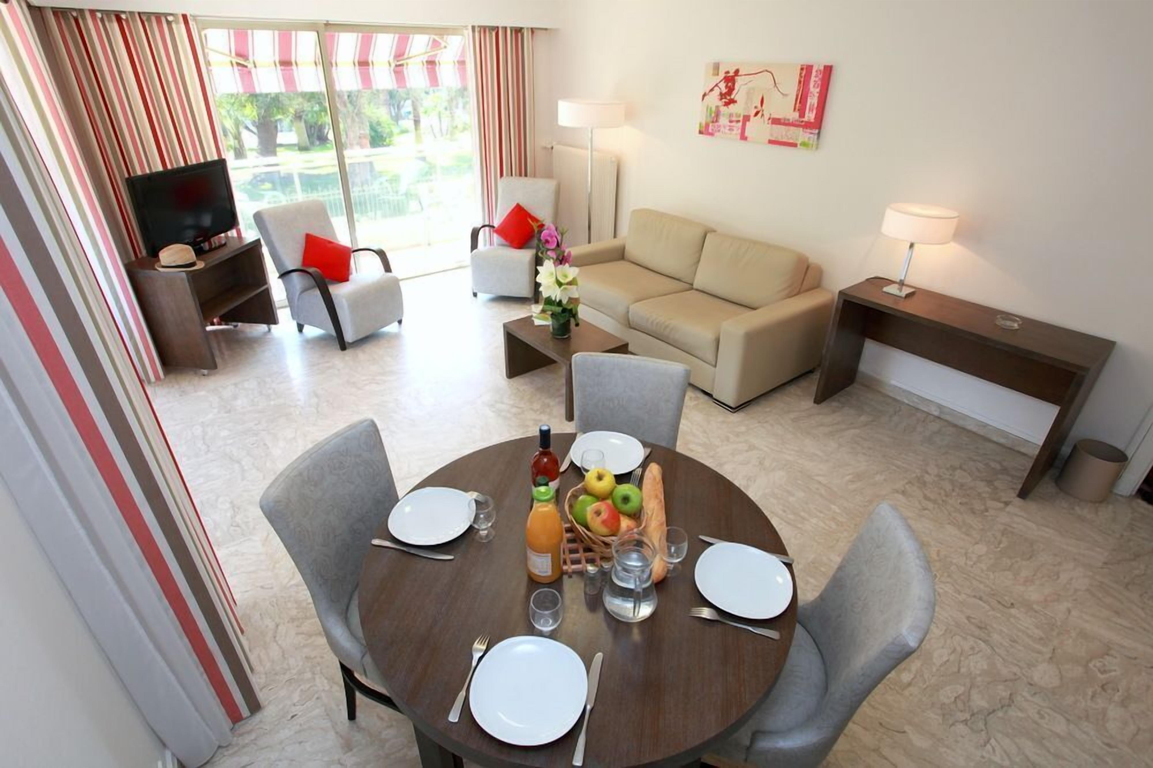 A dining area with a round table set for four, a sofa, a TV, and a lamp.
